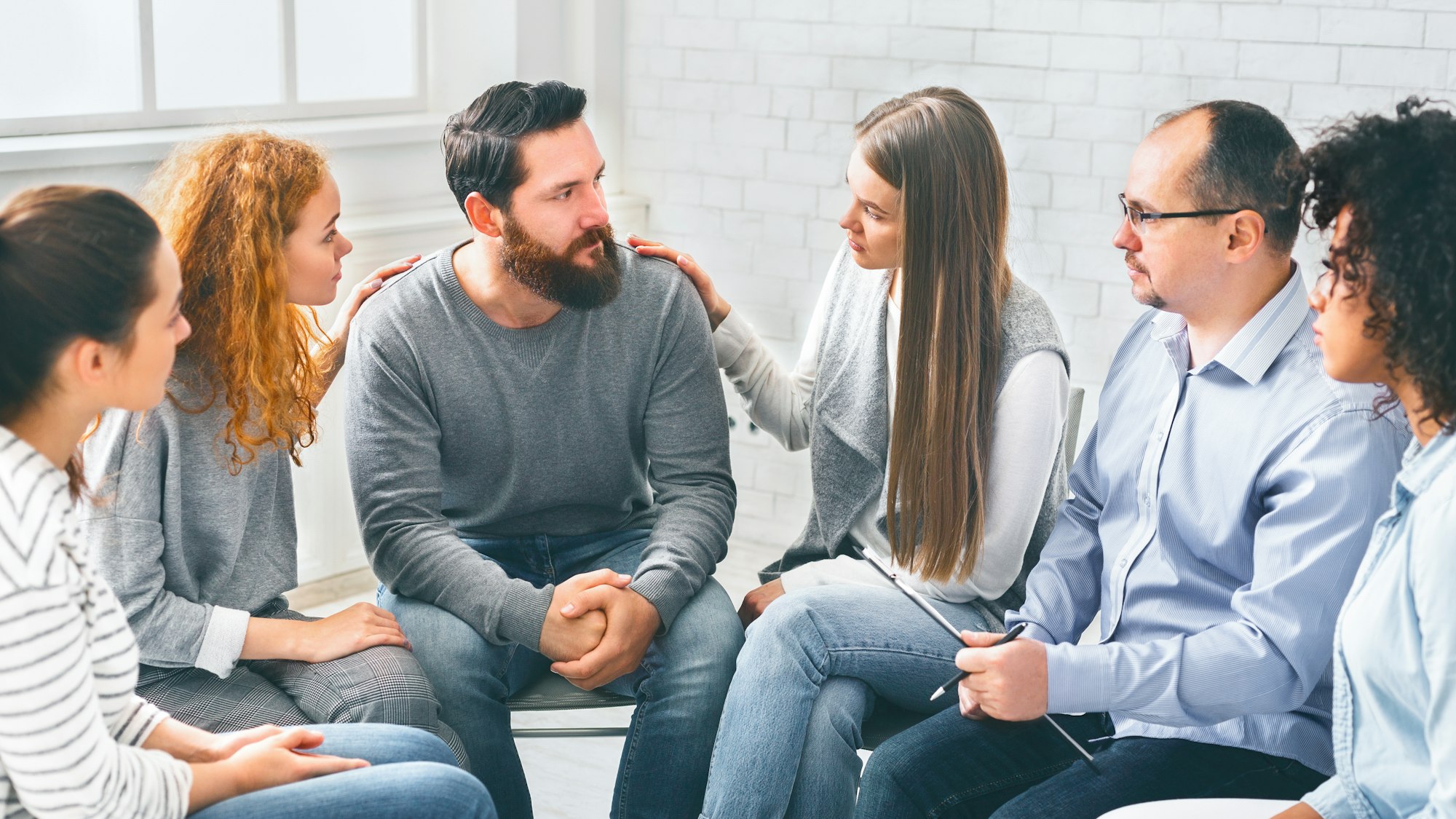 Therapy Group Members Comforting Upset Man On Community Meeting In Rehab